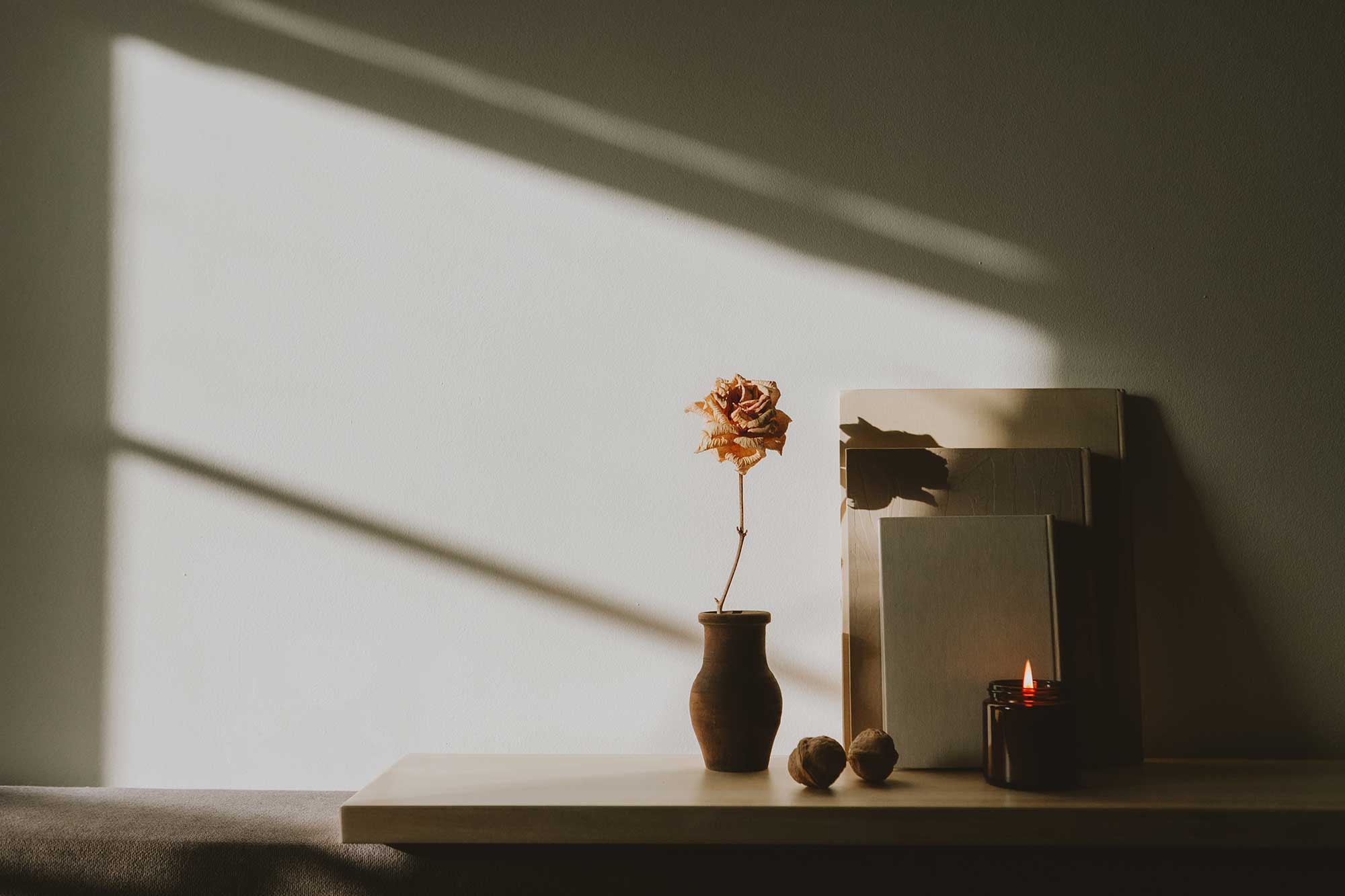 Stillleben mit einzelner Blume in einer Vase, gestapelten Büchern und einer brennenden Kerze im warmen Licht.